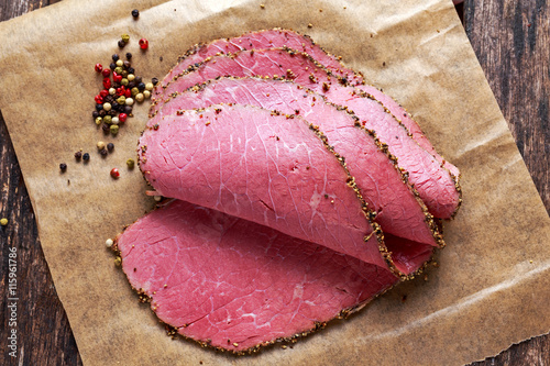 Peppered roast beef pastrami slices on paper with grains of coloured pepper.