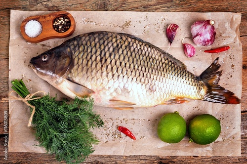 Fresh raw carp fish with lime, dill and garlic on old wooden background.