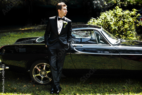 Handsome fiance leans on a shiny black American car