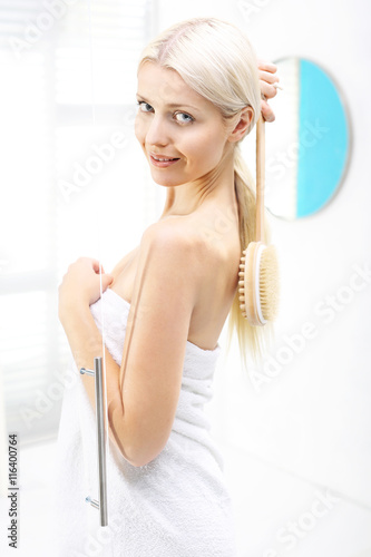 Masaż pleców. Pod prysznicem kobieta myje plecy szczotką na kiju