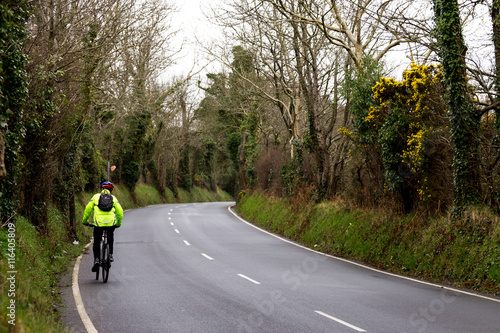man riding a bicycle up a country road in high-visibility jacket 