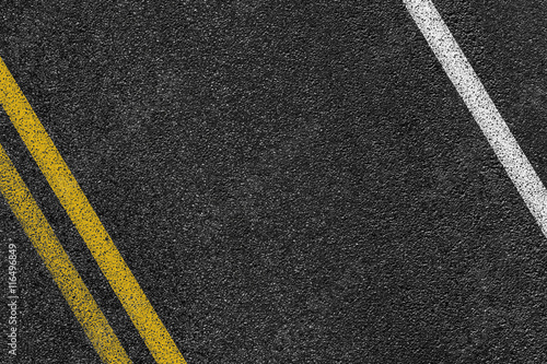 Level asphalted road with a dividing white and yellow stripes. The texture of the tarmac, top view.