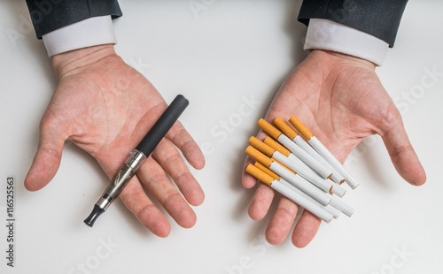 Hands are holding electronic and conventional tobacco cigarettes and comparing them