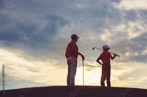 man with his son golfers standing on golf course at sunset, back view
