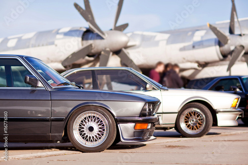 Right front side of two old european sport cars with plane on background