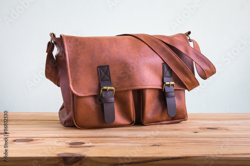Men's accessories with brown leather bags on wooden table over wall background