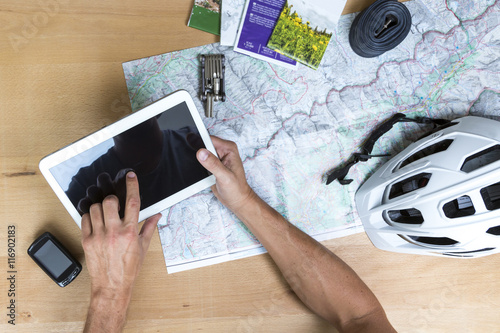 Desk with hands on a map, tablet pc and bike accessoires, elevated view