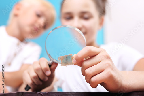 Mika. Dwoje dzieci, dziewczynka i chłopiec oglądają przez szkło powiększające kamienie ze swojej kolekcji skał.