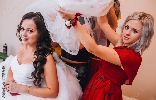 Bride and three bridesmaids in similar red dresses with perfect make up and hair style in a light loft space