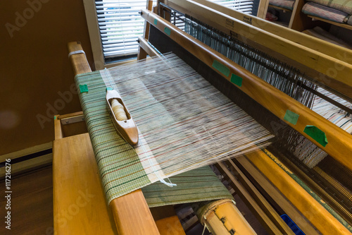  Cloth being woven on a wooden loom, holding the warp threads in place while weft, filling, threads are woven through them creating a green pattern 