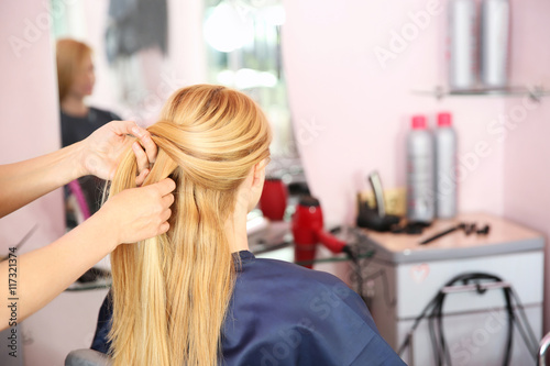 Hairdresser braiding woman's hair in hairdressing salon