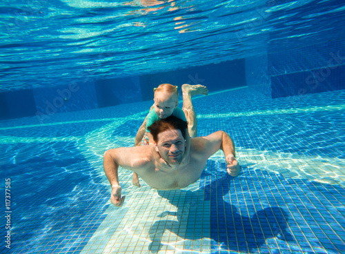Father dives with young daughter. Little girl rides daddy underw