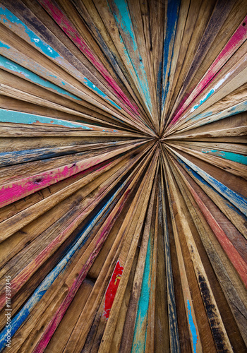 an abstract art image made from distressed, colourful strips of wood that are arranged into a starburst effect with lines converging into a central point.