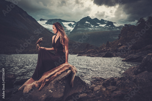 Nordic goddess in ritual garment with hawk near wild mountain lake in Innerdalen valley.