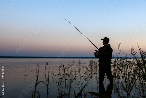 Fisherman silhouette at sunset on the lake while fishing 