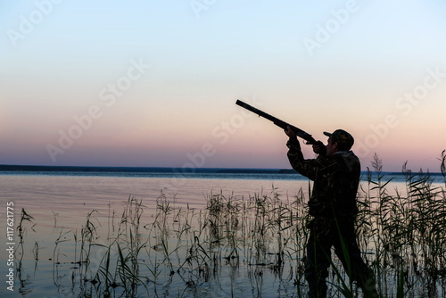 Hunter silhouette at sunset, while hunting on the lake 