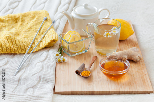 Herbal tea in glass cup with flowers of chamomile, turmeric and honey on a wooden board. Treatment with a cold drink. Treatment of folk remedies in bed. Knitting hobby.