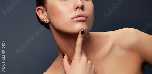 Close-up lips, neck and shoulder of young girl, touching her chic over grey background