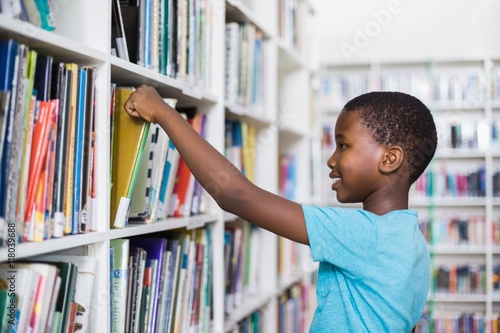 Schoolboy selecting a book from bookcase in library