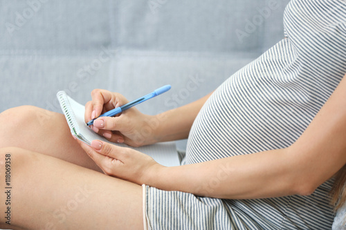 Pregnant woman making packing list for maternity hospital at home