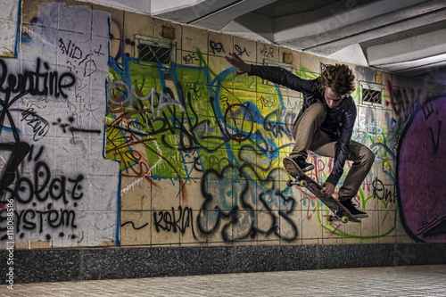Skateboarder doing a skateboard trick against graffiti wall