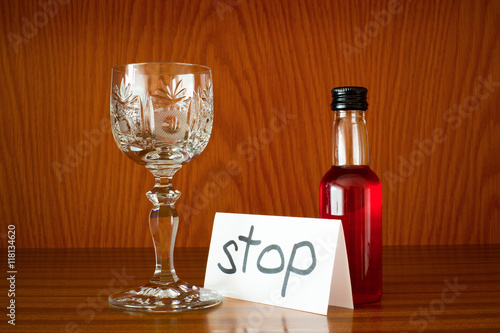 Glass, bottle with alcohol and paper with text STOP. Appeal to overcome addictive alcohol abuse and dependence through detoxifiction, treatment, rehabilitation and abstinence 