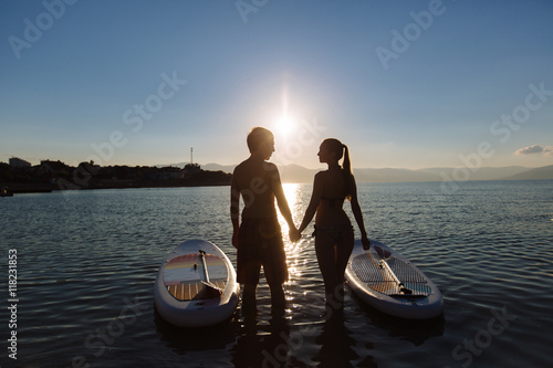 Silhouettes of beautiful couple with sup serf and paddle at the ocean