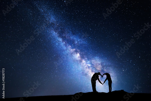 Man and woman holding hands in heart shape on the background of the Milky Way. Night landscape