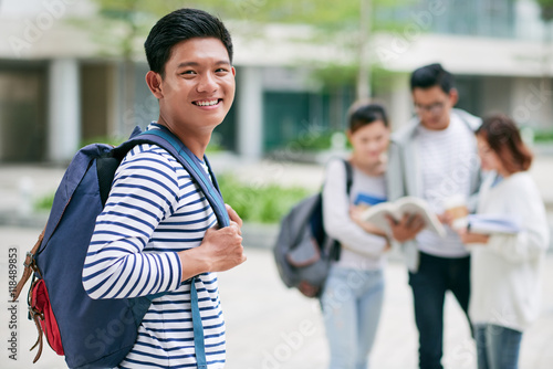 Happy Vietnamese guy with backpack standing on campus