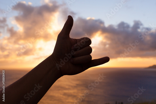 Hand doing Hang loose sign against a beautiful sunset. 