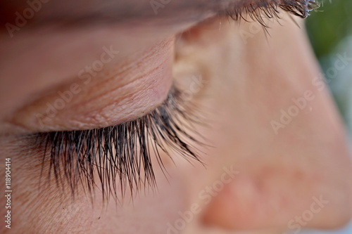 Macro detail of a closed woman eye with extremely long black natural eyelashes and dark brown eyebrows behind the thick sunglasses 