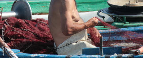 Mani di un vecchio pescatore a lavoro sulla rete da pesca