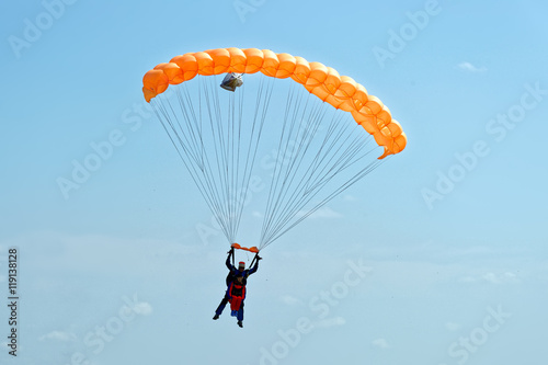 Paraglider flying on orange-colored parachute in blue clear sky at a bright sunny summer day. Active lifestyle, extreme hobbies