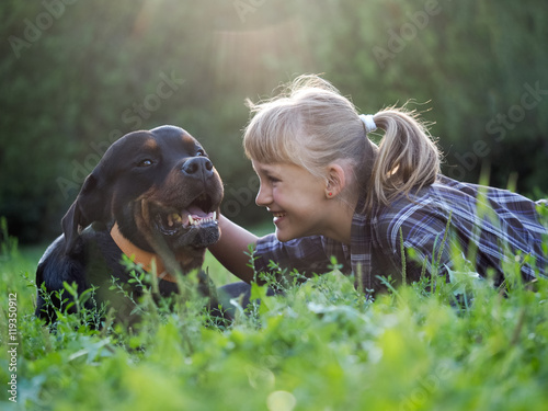 Happy girl and dog in the sunshine. The dog is big and scary - Rottweiler. Green grass, park, sunset