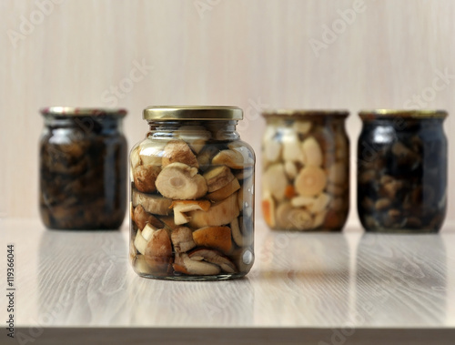 Glass jars with marinated mushrooms on a light wooden background. Close-up.