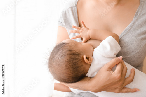 Mother breastfeeding her newborn baby beside window