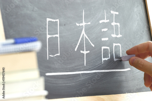 Hand writing some the word "Japanese" in kana syllabary on a blackboard in a Japanese class. Some books and school materials.