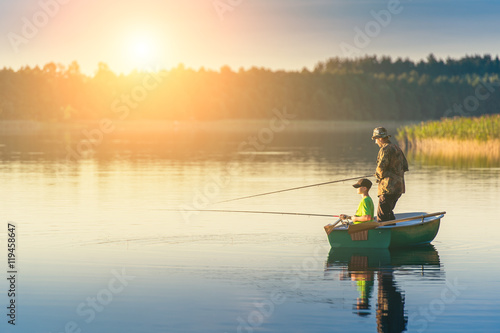 father and son catch fish from a boat at sunset