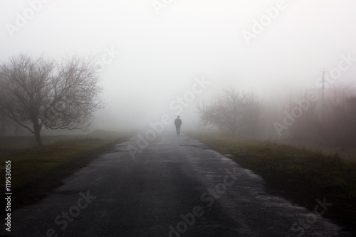 Wayfarer in fog. Silhouette of man walking on misty village road. Homecoming. Loneliness, .nostalgia, sad mood