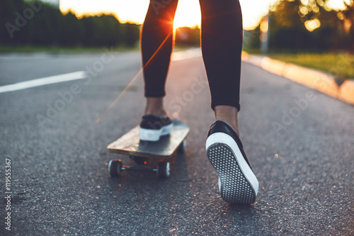 young skateboarder legs riding on skateboard in front of the sun