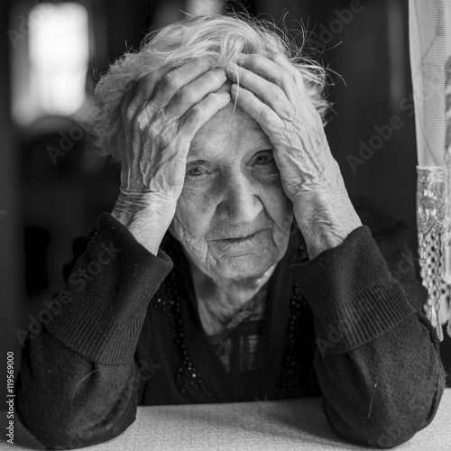 Sad elderly woman holds hands a head. Black and white photo.