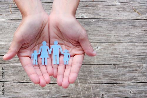 Paper family in hands on wooden background welfare concept