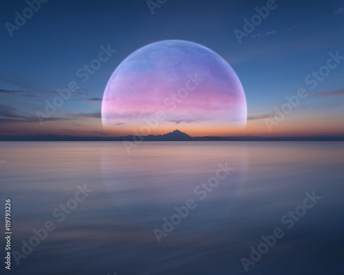 Pink planet like moon above the ocean and mountain