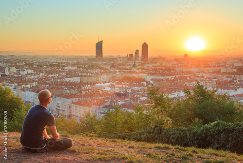 Man sitting in the grass and enjoying the sunrise over the city of Lyon, France.
