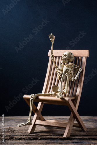 skeleton is gesticulate sitting on the wood chair