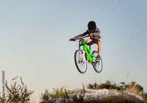 Bicyclist in helmet and glasses high jump on a mountain bike on the hill against blue sky in the mountains. Downhill cycling. Extreme sport.