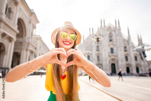 Young and happy tourist showing heart with hands in front of the famous Duomo cathedral in Milan. Happy vacations in Milan