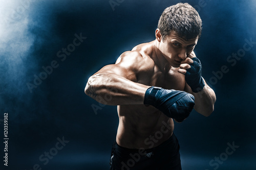 Muscular kickbox or muay thai fighter punching in smoke.