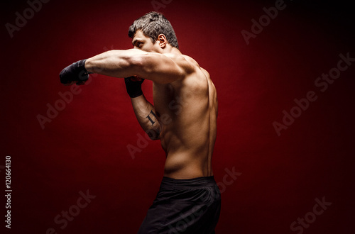 Studio portrait of handsome muscular fighter practicing boxing on red background