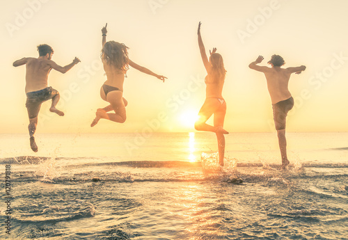 Group of happy people jumping in the sea at sunset.